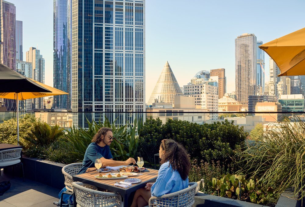 A couple dining on share plates on a rooftop overlooking the city skyline.