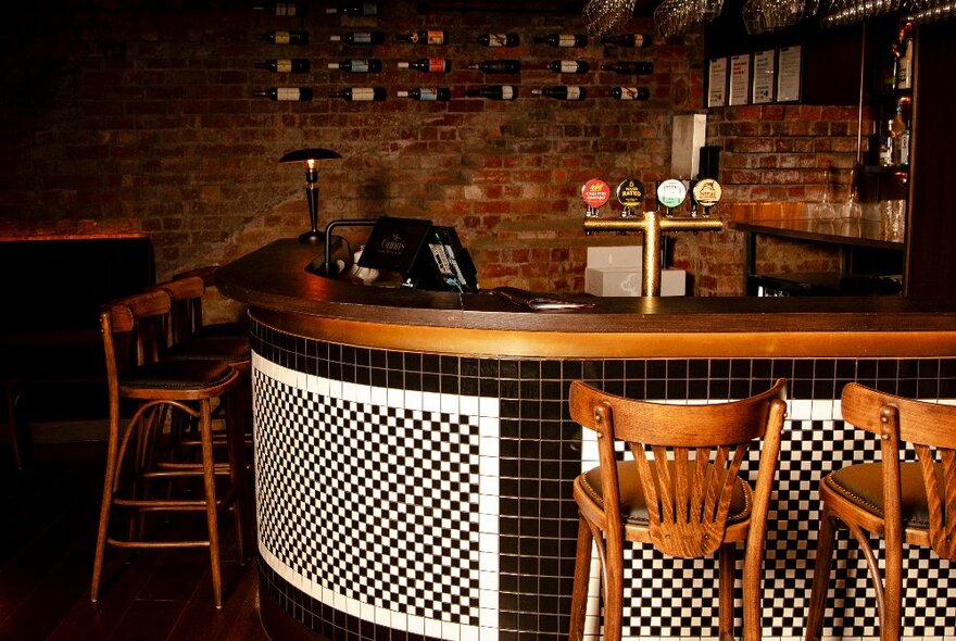 A very small corner bar with wooden stools and a tiled chequerboard pattern.