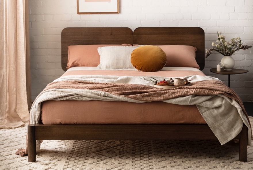 A chocolate coloured bed with brown toned bed linen.