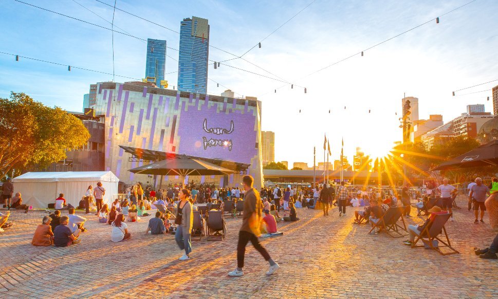 People are watching a screen in a city square at sunset