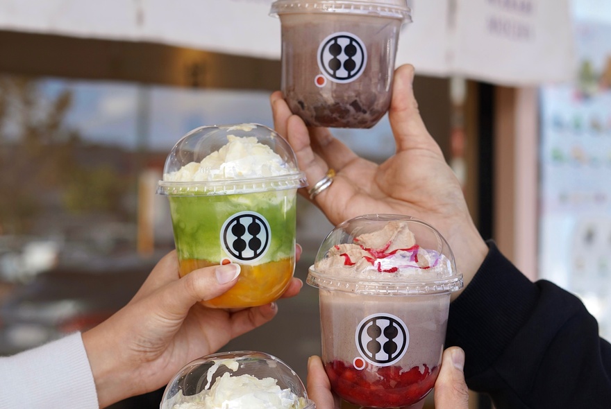 Hands holding cups of Japanese dessert including matcha and chocolate.
