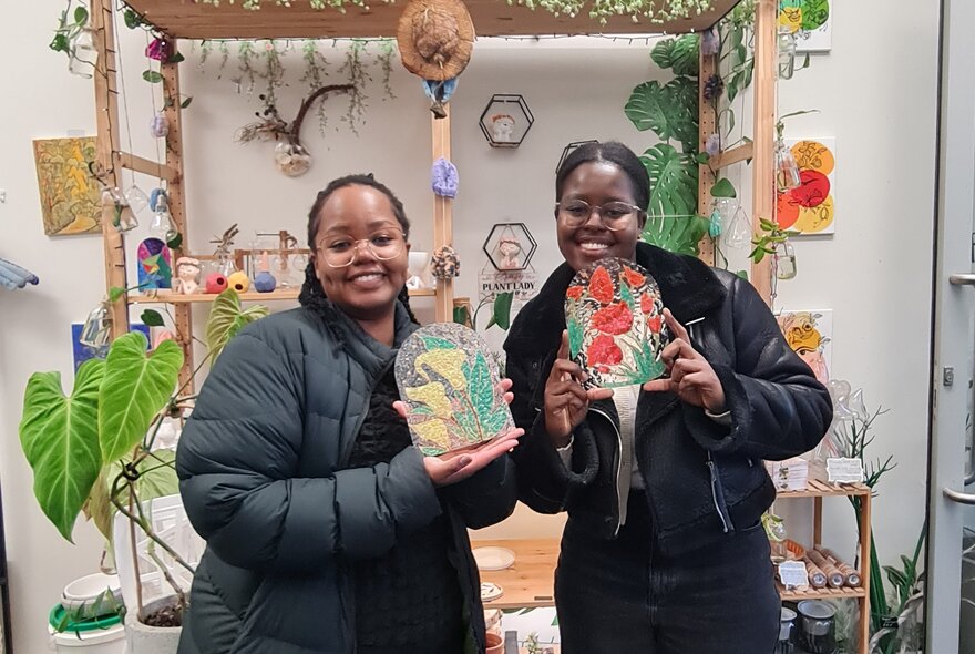 Two people smiling and holding up hand painted glass lamps that they have made.
