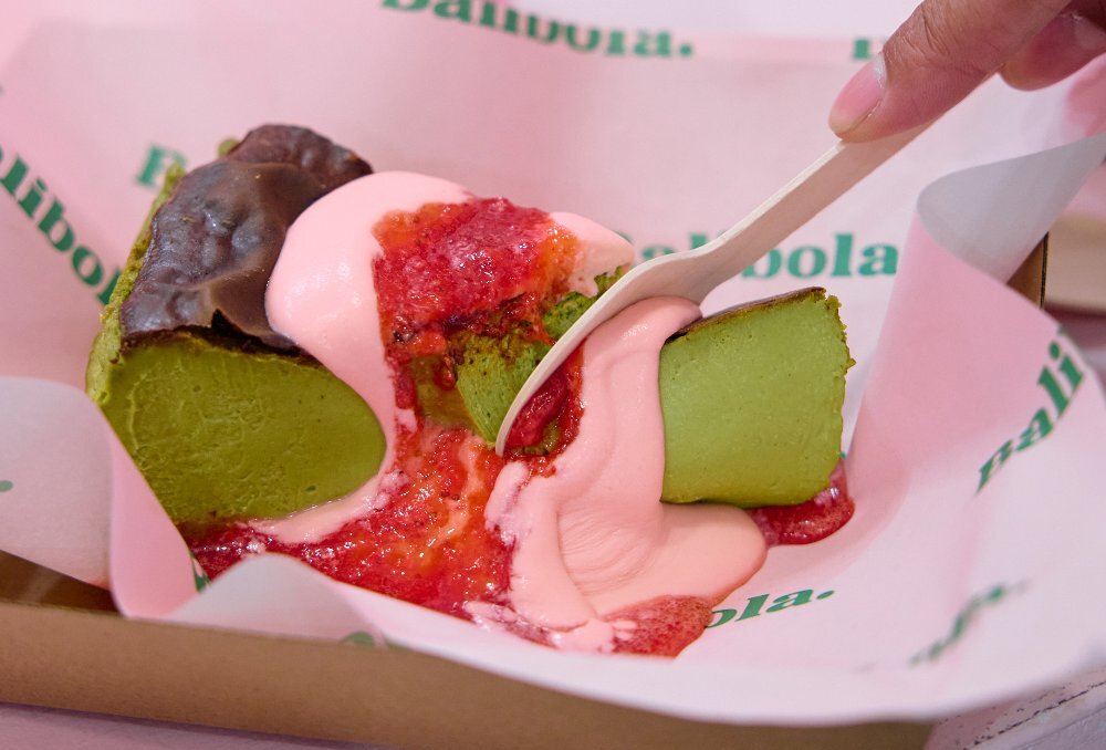 A person is cutting into a matcha cheesecake topped with strawberry sauce and jam.