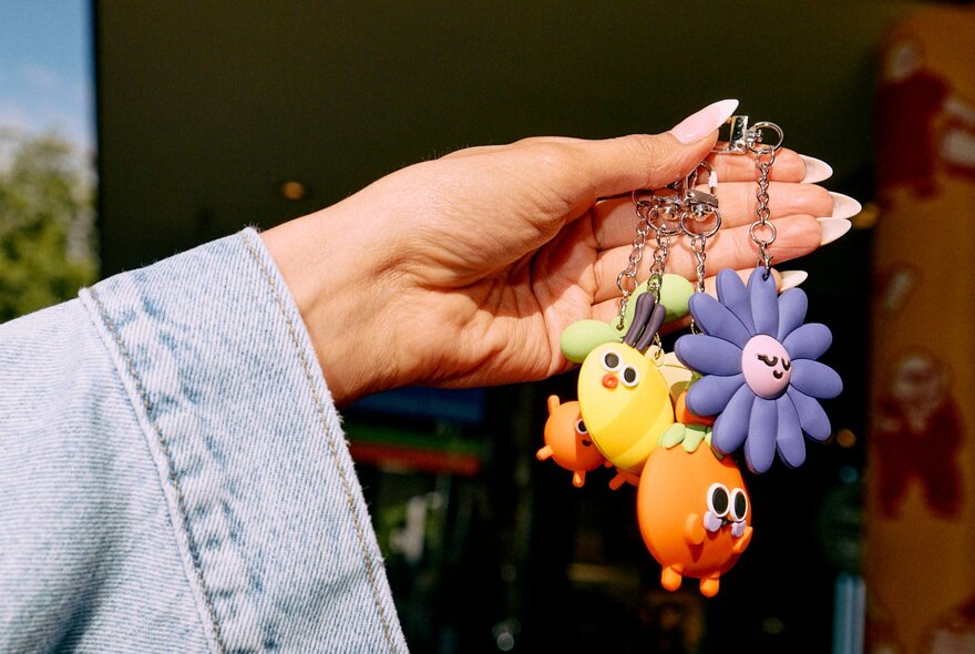 Hand holding several colourful bag charms.