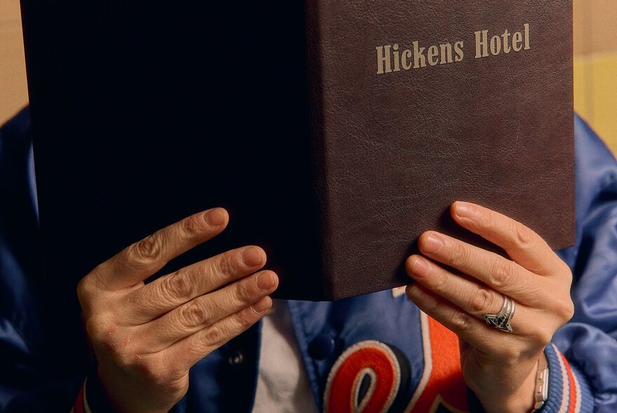 The menu at Hickens Hotel, being held by two hands, a person in a bomber jacket hidden behind it.