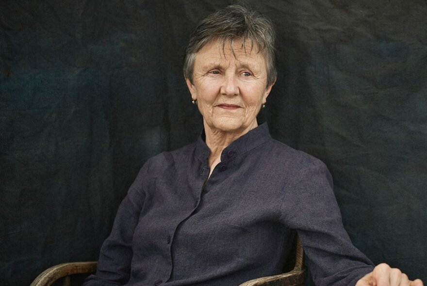 Author Helen Garner sits in a black shirt against a black background. 