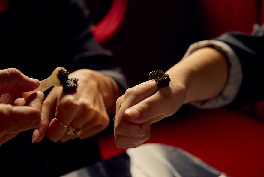 Spoon placing caviar on two pairs of hands.