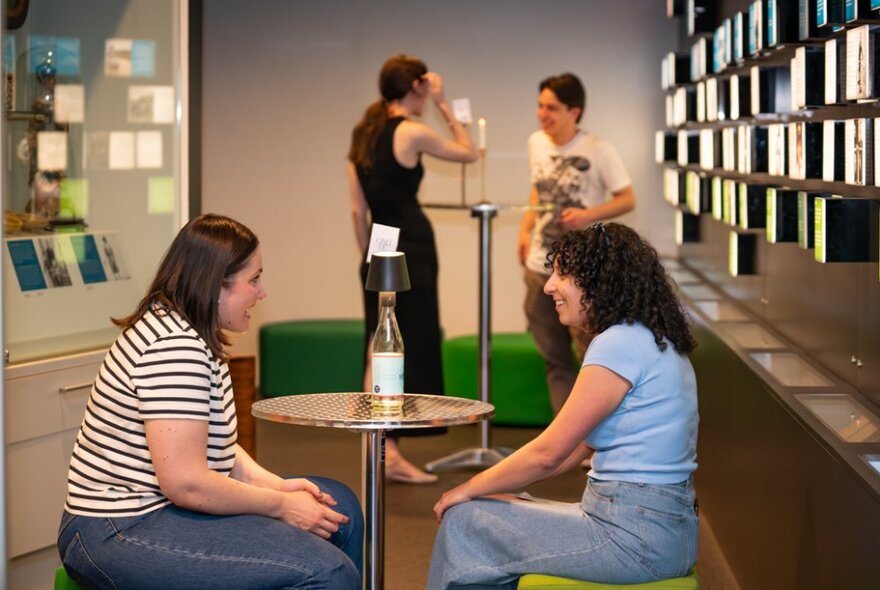 People talking together over a bottle of wine in a workroom with bookshelves.