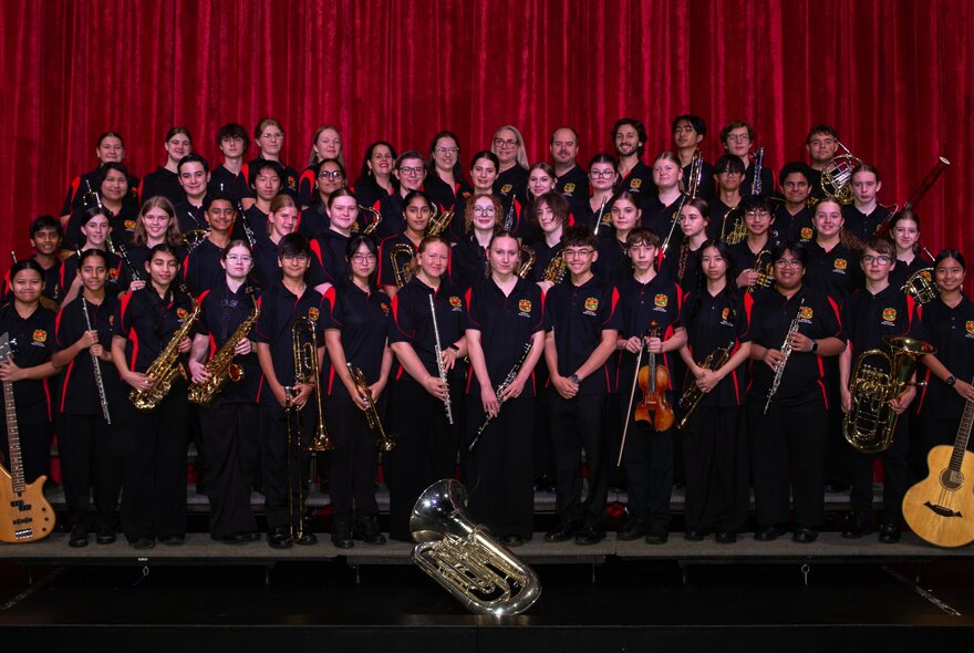 La Salle College Concert Band assembled for a group shot on stage in front of a red curtain. 