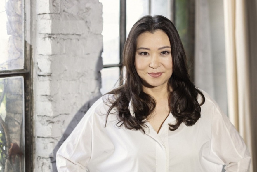 Conductor Shiyeon Sung wearing a white shirt, standing in front of windows.