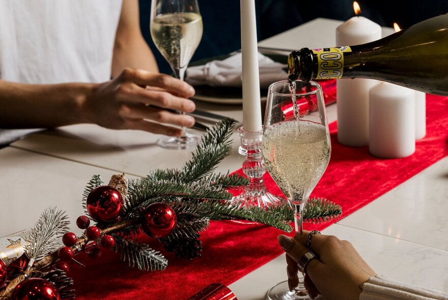 Christmas decorations on a table and champagne being poured into a glass.