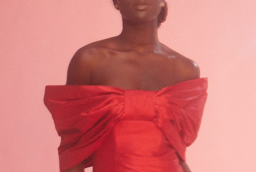 A fashion model wearing a strapless red dress against a pale pink background.