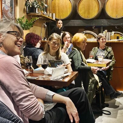 A group of people in a cosy restaurant with wine barrels lining the walls. 