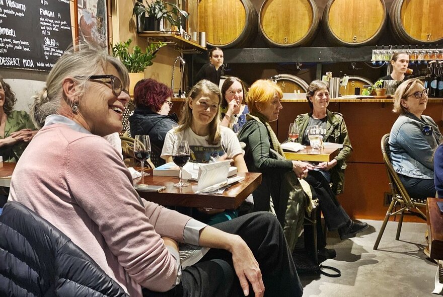 A group of people in a cosy restaurant with wine barrels lining the walls. 