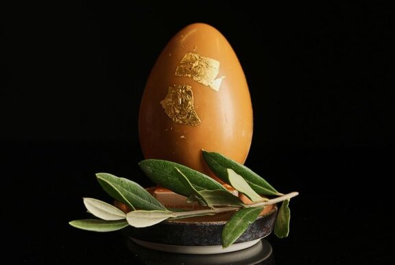 A large caramel chocolate egg with 24 karat gold leaf, resting on a small platter with a sprig of a native Australian bush.