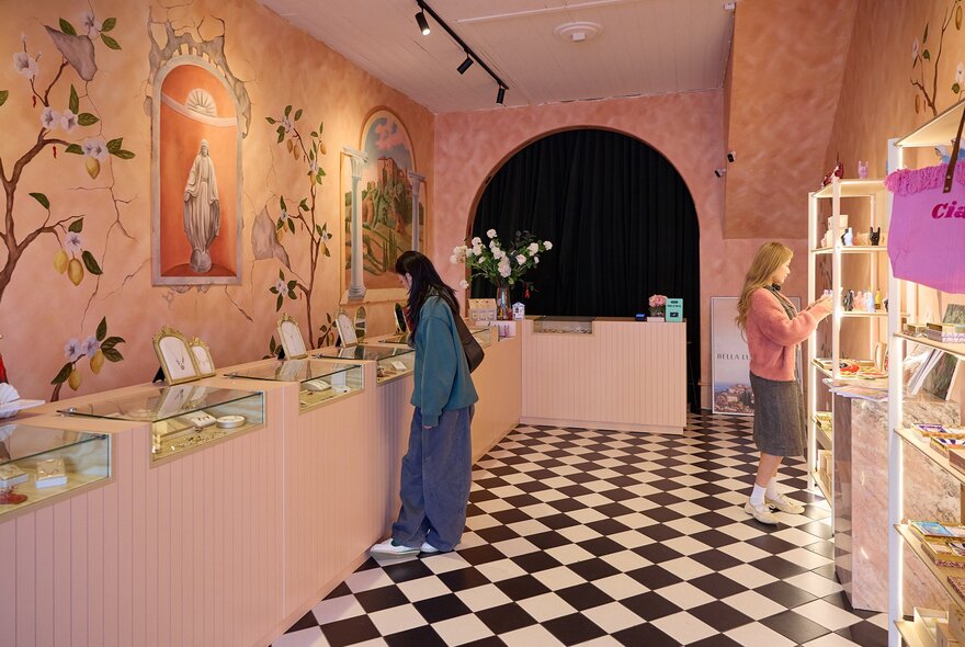 A woman browsing in a pink jewellery store with checkerboard floors and an Italian mural on the wall.