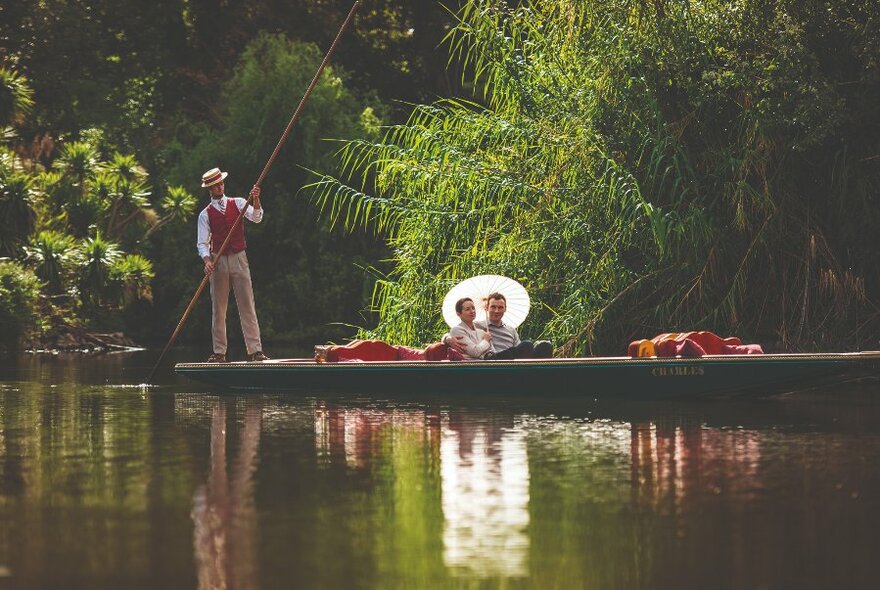 A seated couple holding a parasol and a guide punting on the lake at Royal Botanic Gardens. 