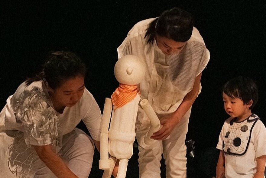 Performers wearing white, standing with a model of a child and a small child wearing a bib.