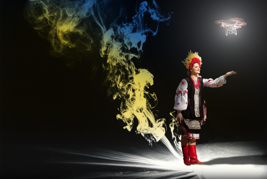 A dancer in Ukrainian traditional dress on stage with a puff of blue and yellow smoke behind them. 