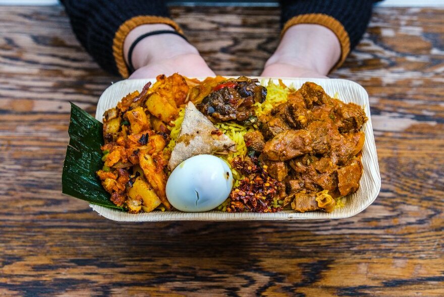 Hands holding a takeaway plate of Sri Lankan food.