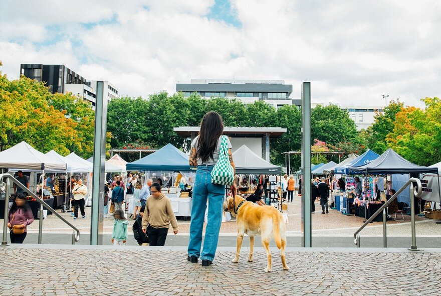  A woman and a golden retriever walking into an outdoor market.