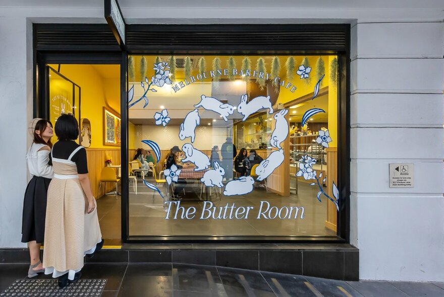 Two people about to walk through the door of a cafe with rabbits and signage on the window.