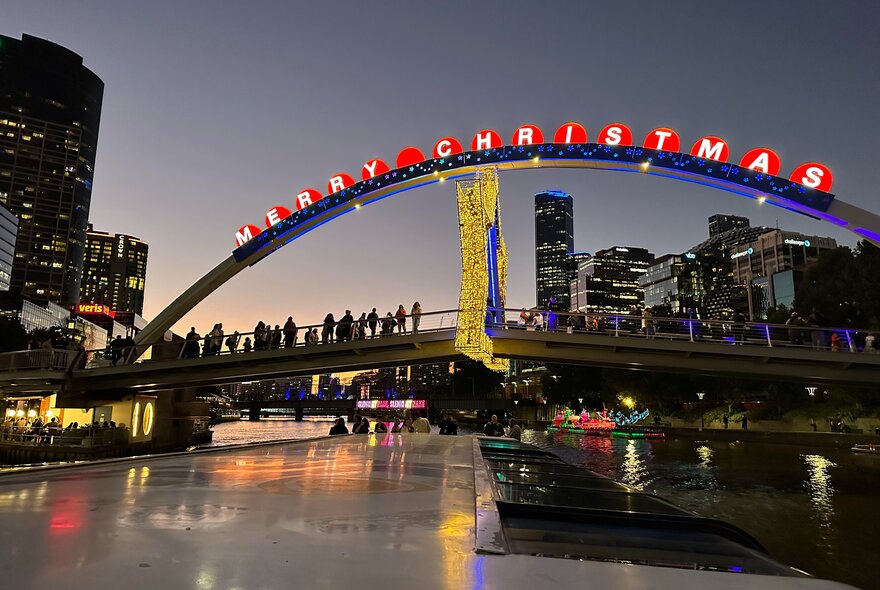 An illuminated Merry Christmas sign on top of a bridge over the Yarra, at nighttime.