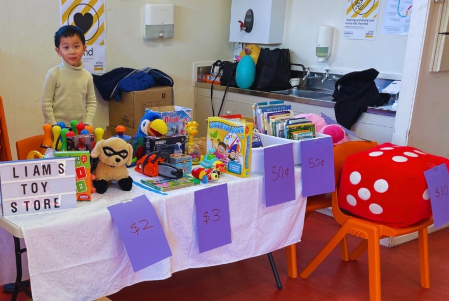 A child manning a stall with colourful toys, books and games.