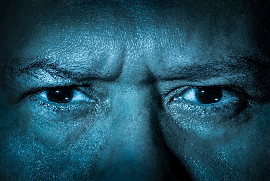 A blue-tinged close up of a man's face, showing anger in his eyes.