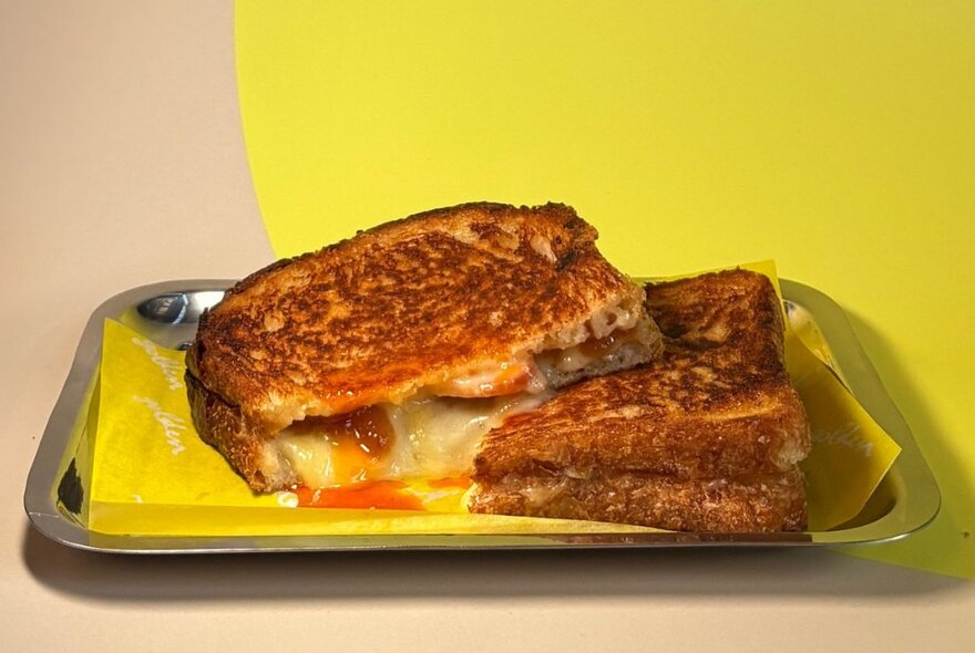 A melting cheese toastie on a silver tray with serviette.
