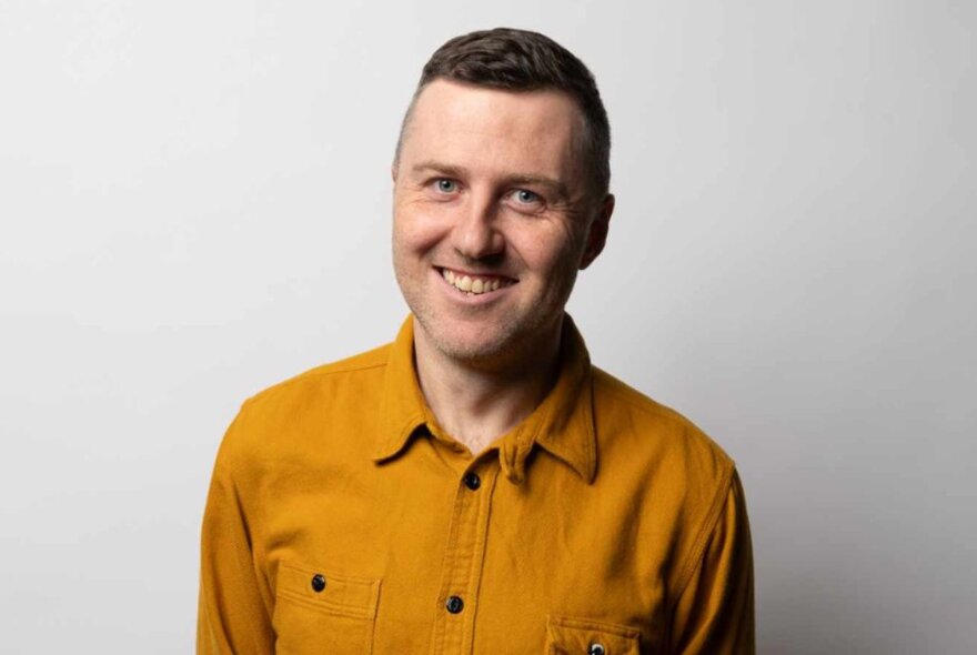 A smiling Lloyd Langford wearing a mustard coloured shirt. 