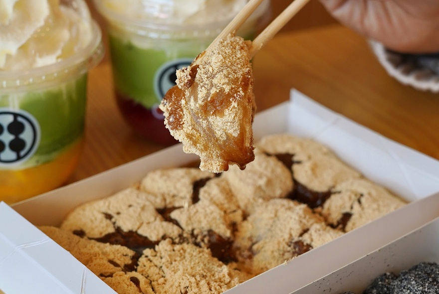Chopsticks picking up Japanese wagashi dessert with syrup, served in a box.