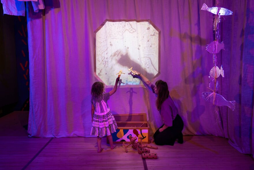 An adult and a young child interact with an ocean-themed shadow puppet screen; part of an interactive installation at ArtPlay.