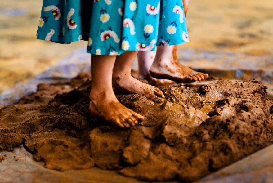 Two pairs of child's feet squishing into brown mud.