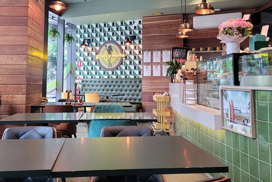 The interior of a cafe, with a green tiled front counter, 1950s style vinyl swivel chairs and square dining tables.