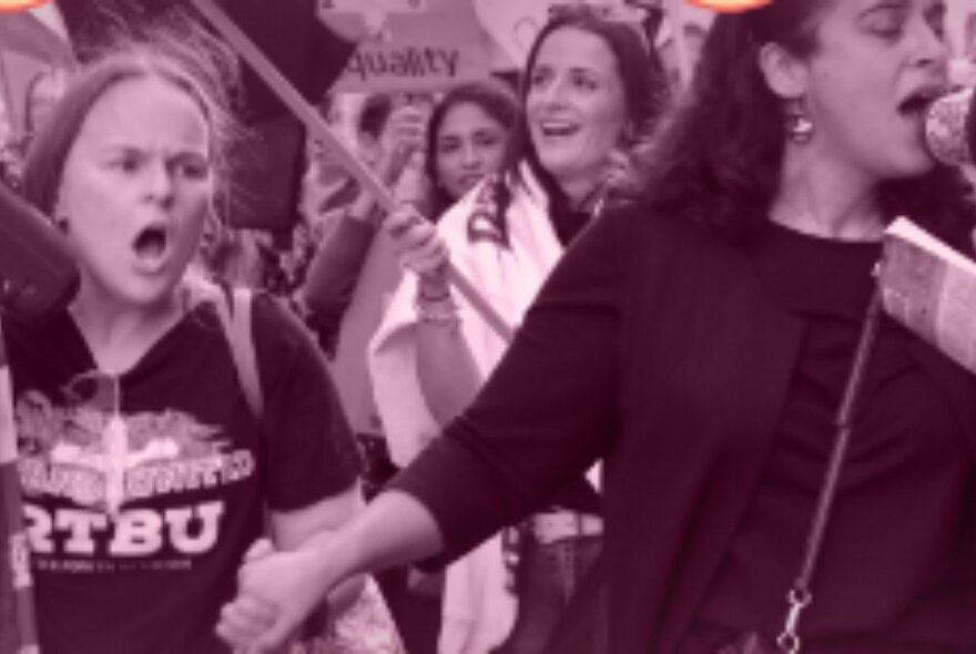 Sepia-toned image of women walking hand in hand at a demo with flags and logos.