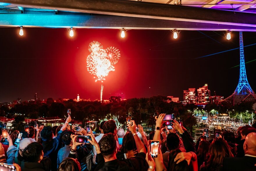 Crowds on a terrace watching fireworks with Arts Centre spire illuminated.