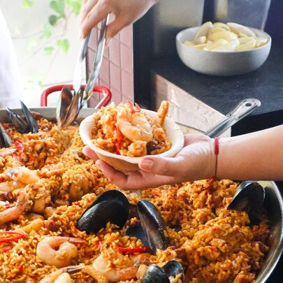 A chef preparing a bowl of seafood paella from a large pan.