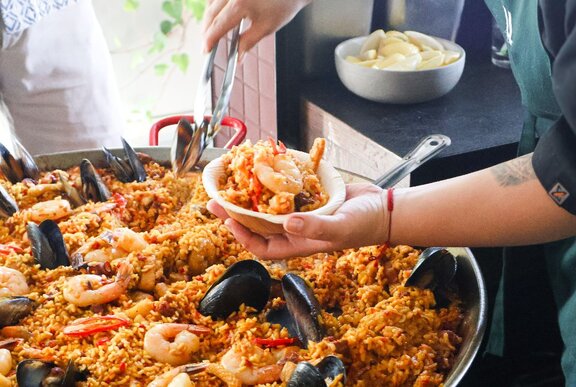 A chef preparing a bowl of seafood paella from a large pan.