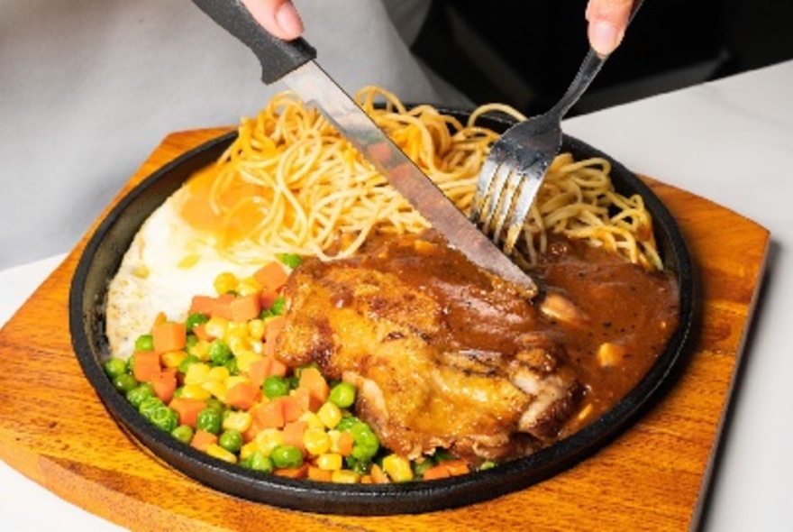 Knife and fork cutting into a plate of chicken and noodles.