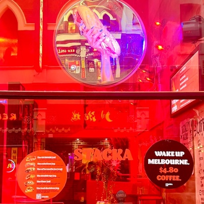 Exterior of Stacka shopfront, with large signs on the window and a view into a warm red coloured interior.
