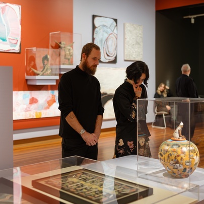 Two people in black in a gallery space looking at artefacts under glass cases.