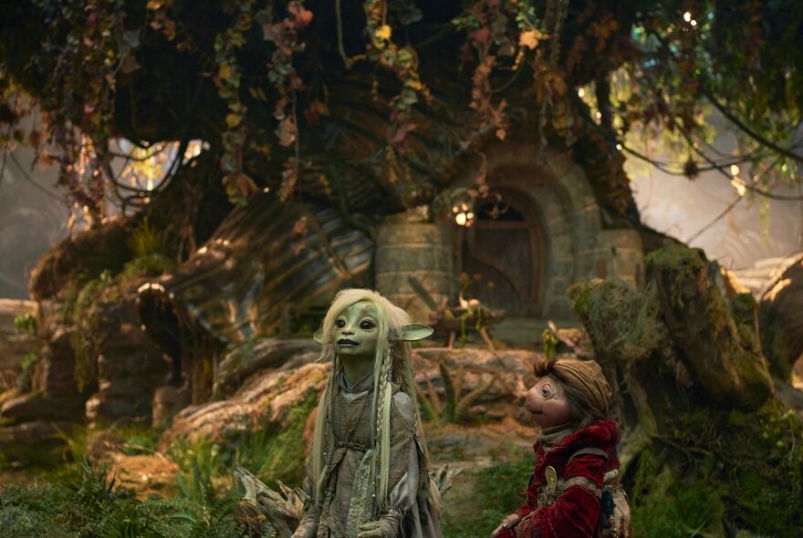 A still image from a film with fairy creatures in front of a large tree with a door.