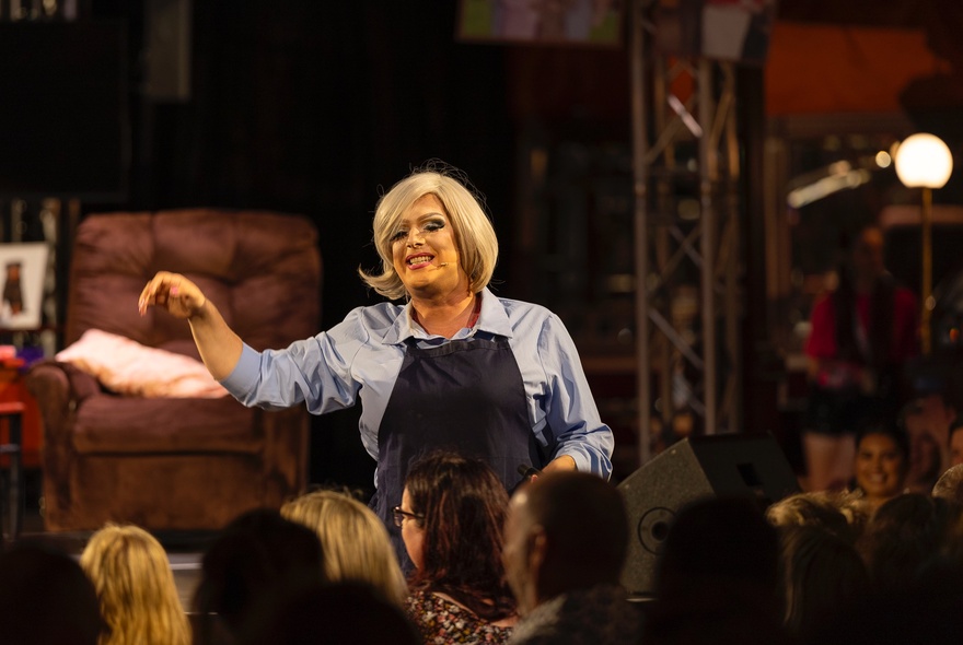 A cast member from the musical 'A Fountain Lakes Christmas Carol: A Drag Parody Play', performing on a stage in front of an audience.