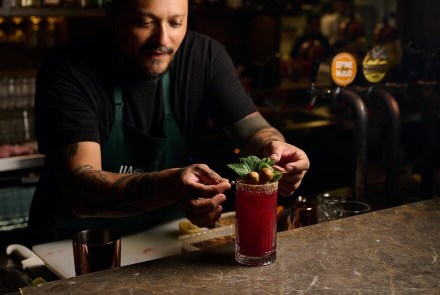 A bartender garnishing a tall red cocktail at a bar. 