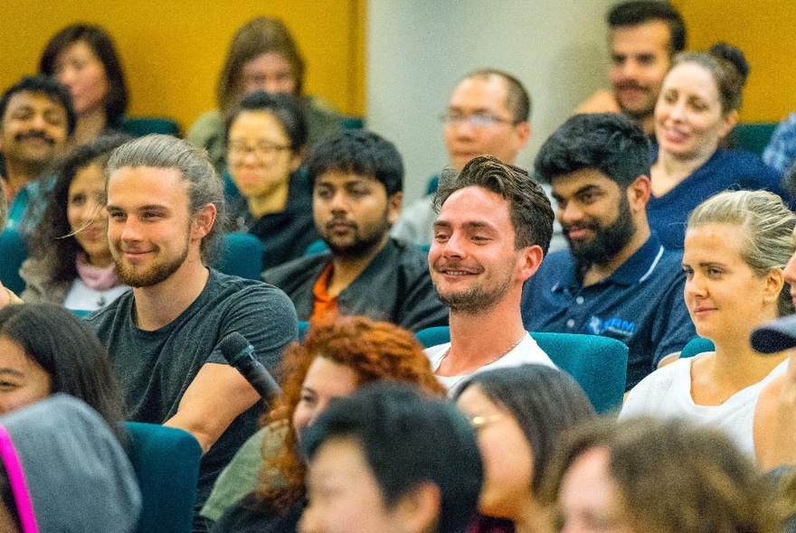 Participants in a happiness workshop seated in an auditorium, many smiling.