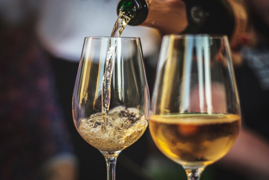 Two wine glasses of champagne, one being poured.