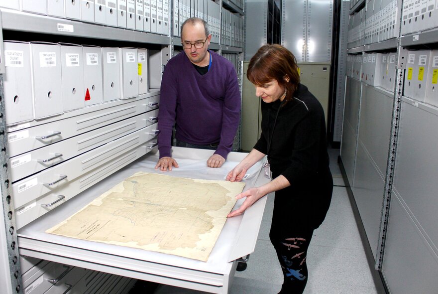 Two people looking at an archival map in a large metal draw.