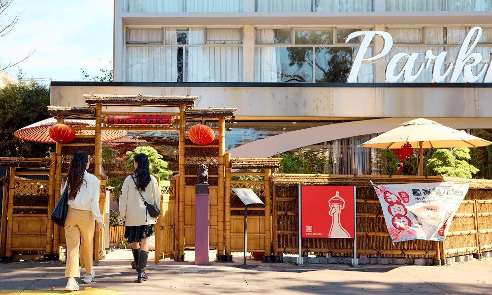 Two women walking into a hotel restaurant under an archway with red lanterns.