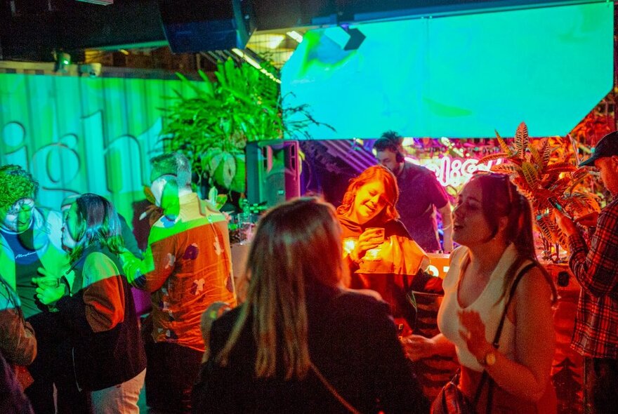 People dancing and socialising at an outdoor bar while a DJ performs in the background. 